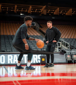 Hunter Glascock stands in a basketball court, watching a player dribble.