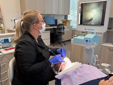 A dental hygiene student sits on a stool, working on a patient who is reclined in a dental chair. The student is looking at the PerioView.