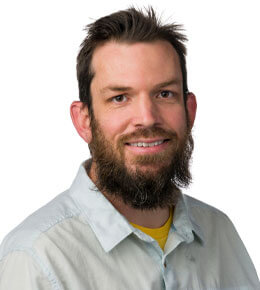 Jeff Wesner sits for his headshot photo. He is wearing a white polo shirt and is smiling at the camera.