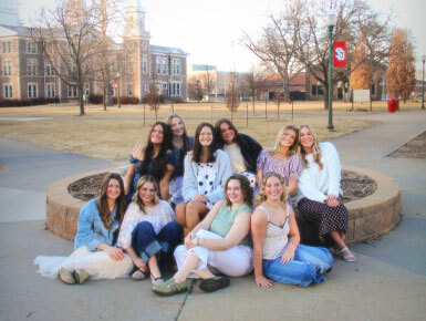 Ten USD students sit in the middle of the USD campus for a group photo. They are members of the Panhellenic Association, which oversees the USD sorority community.