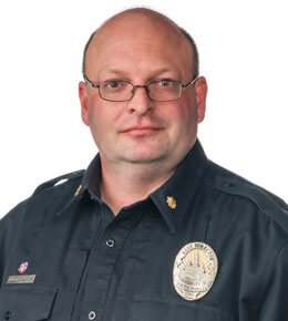 Juston Sangster, assistant chief of police for the University of South Dakota’s University Police Department, smiles at the camera for his professional photo. He is wearing a police officer uniform.