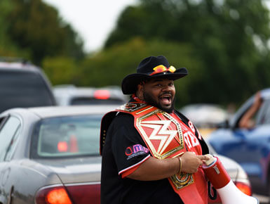 Marcus Destin stands in a parking lot on USD move-in day. He is holding a megaphone and smiling.
