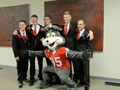 Kyle Schoenfelder stands with friends and poses with Charlie Coyote. They are dressed in tuxedos.