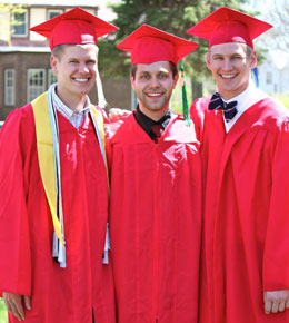 Kyle Schoenfelder stands with friends at his USD graduation. They are dressed in red graduation regalia.
